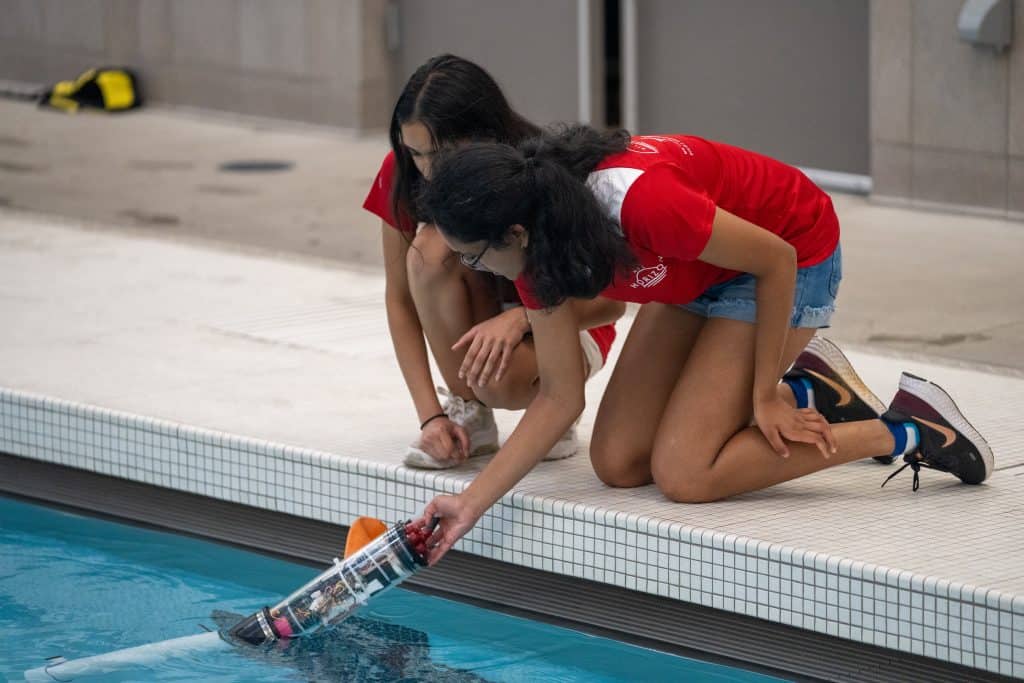 Two female students place their ROV into the pool. 
