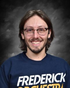A smiling person with long hair and glasses wears a blue sweatshirt with "Frederick Orchestra" printed on it.
