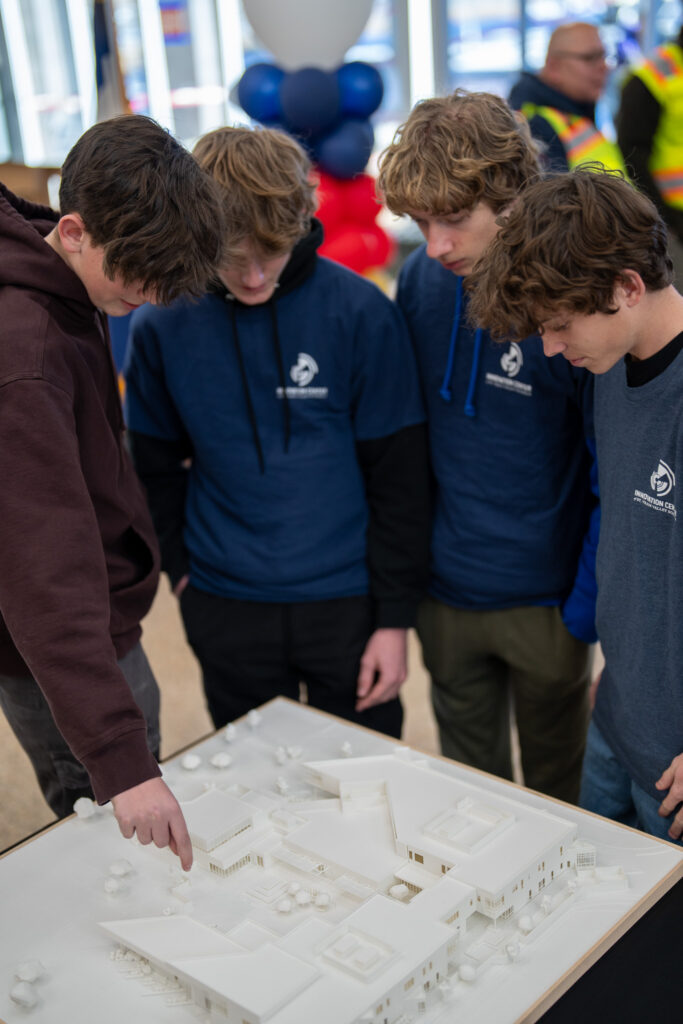 Four young people examine a detailed architectural model on a table, discussing its features.