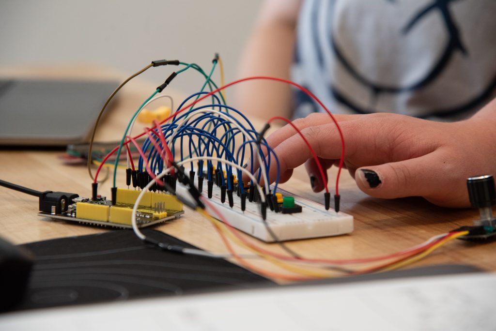 Una mano conecta los cables de una placa de pruebas a un microcontrolador, mostrando la configuración de un circuito sobre una mesa de madera.