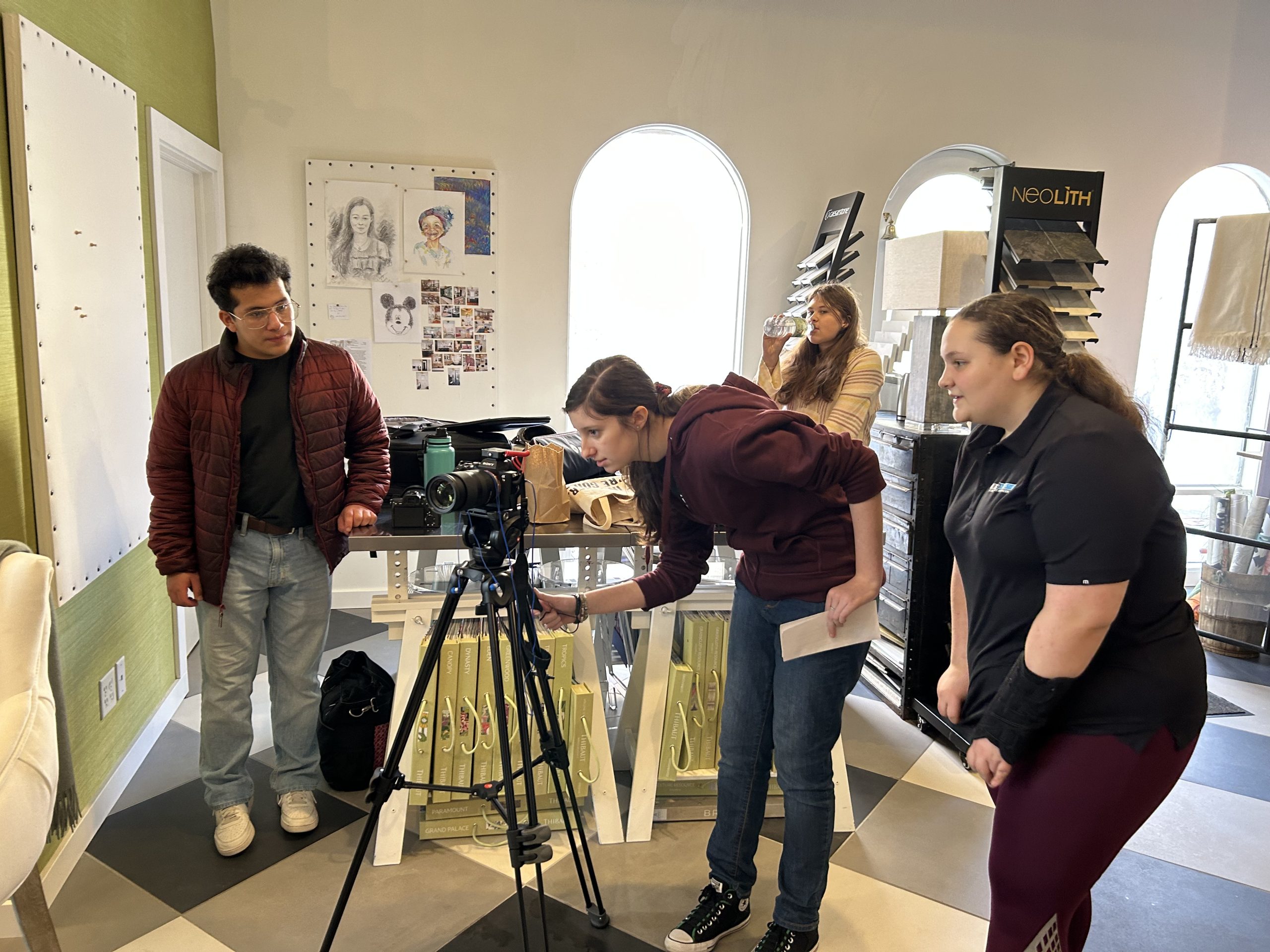 Team members collaborate around a camera setup in a creative workspace, with art and materials visible in the background.